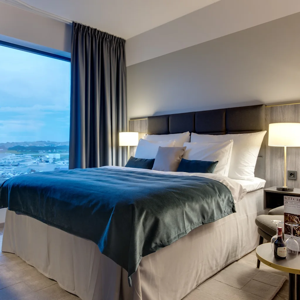 A comfortable hotel room featuring a large bed, a window overlooking a snowy outdoor scene, and a seating area with wine and a menu.