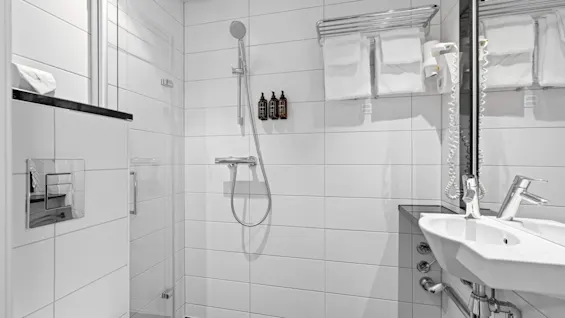 Et rent og moderne bad på Home Hotel Gabelshus med dusj, vask og toalett, med hvite fliser og friske håndklær.
