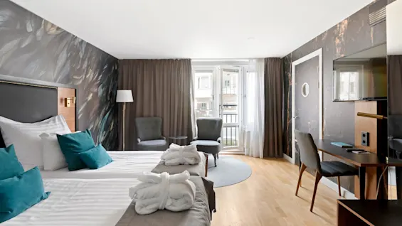 A modern hotel room with a large bed, two armchairs, and a balcony.