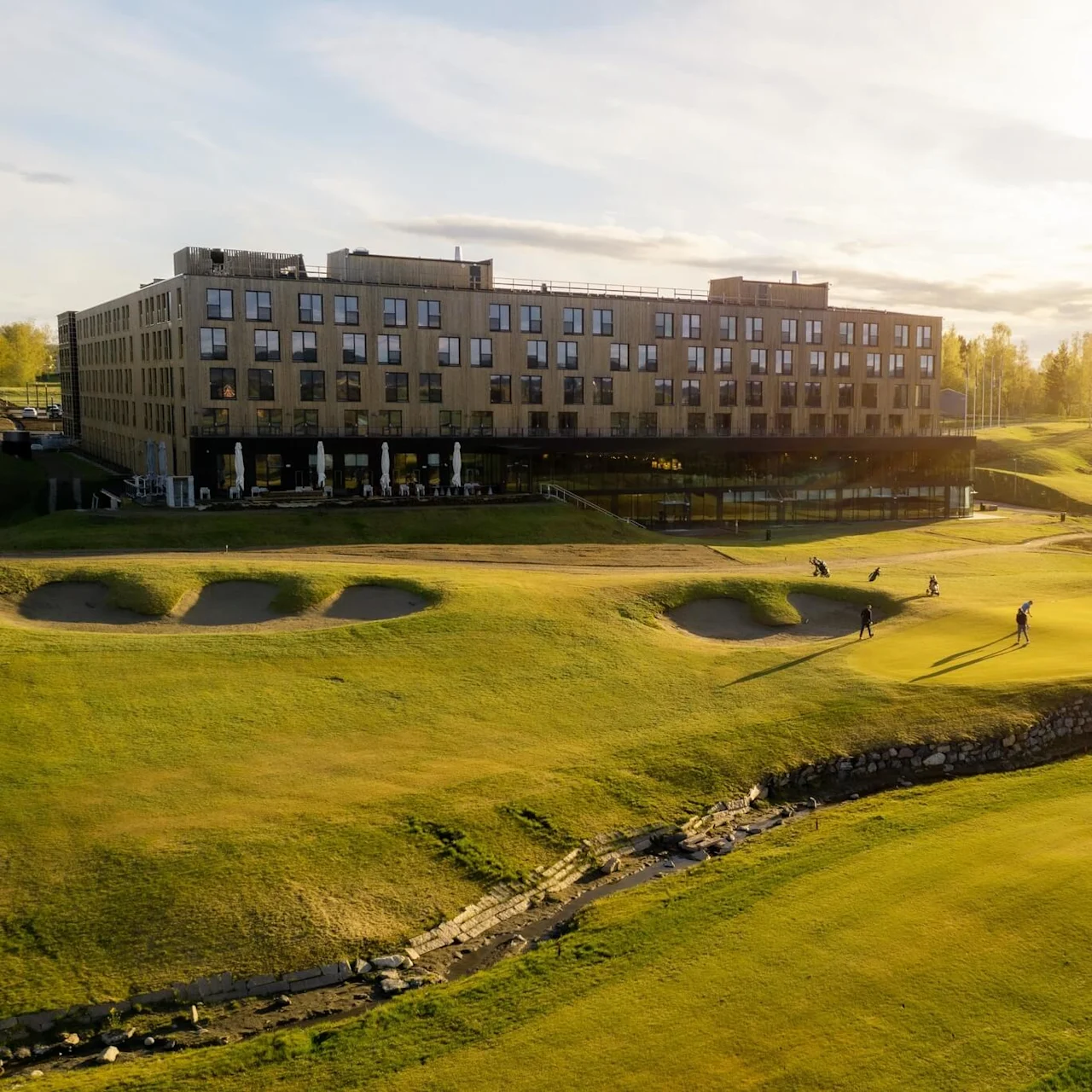 Golfspelare på en bana nära en modern byggnad i solnedgångsljus.