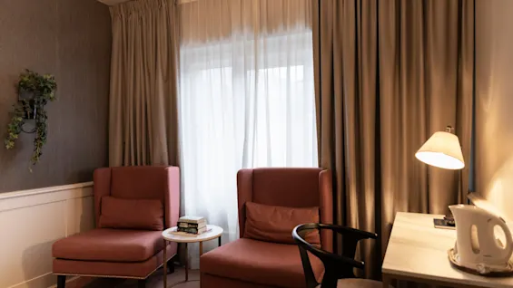 Home Hotel Grand Bodø: A cozy room with two armchairs, a small table with books, and a desk with a lamp and kettle.