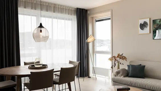 Moderni ruokailu- ja oleskelutila, josta on näkymä vesistöön. Siinä on puinen ruokapöytä, sohva ja moderni valaistus.