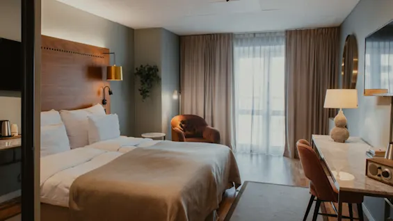Et hyggeligt hotelværelse med en komfortabel seng, et funktionelt skrivebordsområde og blød belysning, perfekt til afslapning eller arbejde.