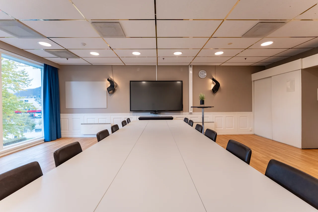 Moderni kokoushuone, jossa on suuri näyttö, valkotaulu ja ikkunanäkymä, jossa näkyy teksti BRUTER.