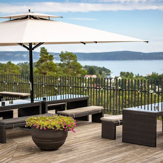 Utendørs terrasse med trebord og benker under en stor parasoll med utsikt over et vakkert landskap