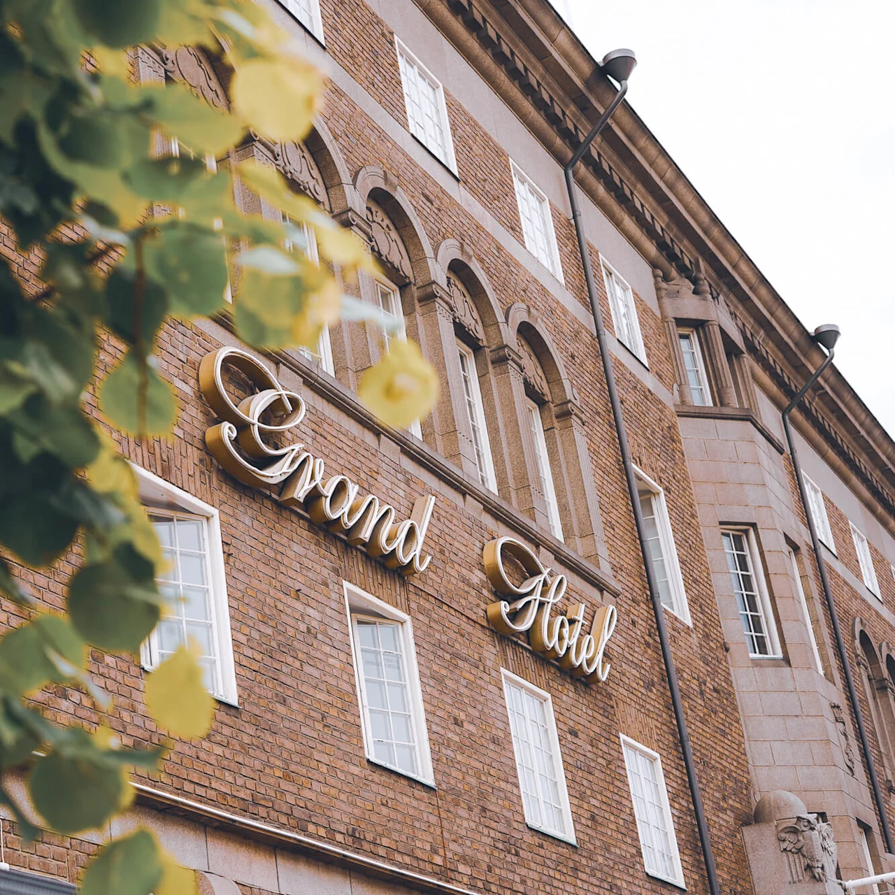 En mursteinsbygning med skiltet "Grand Hotel" innrammet av uskarpe blader.