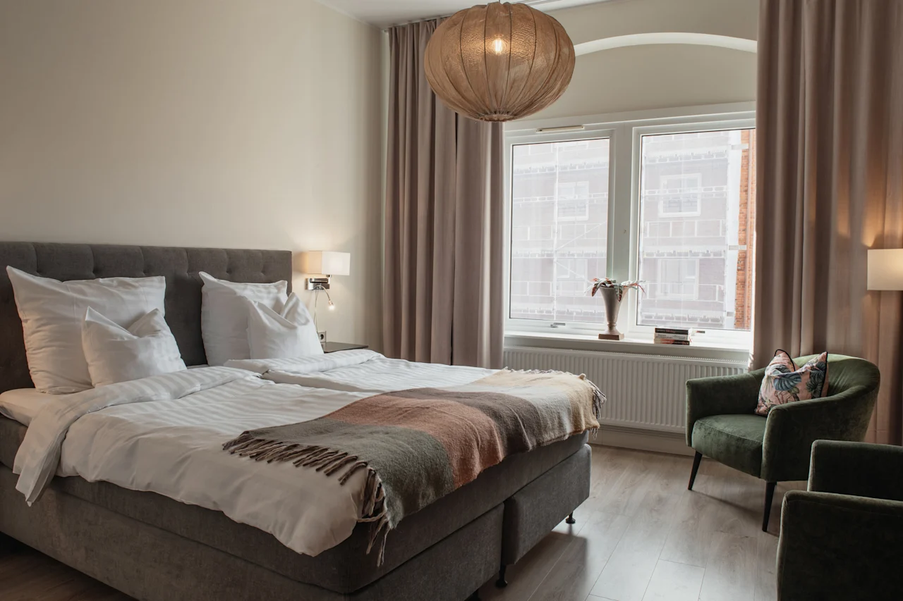 Et hyggeligt hotelværelse på Home Hotel Norre Park i Halmstad med en komfortabel seng, to grønne lænestole og et stort vindue.