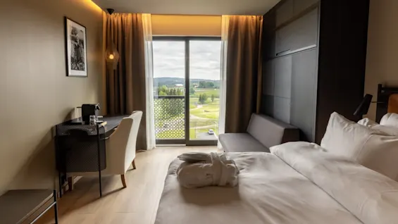 Ett modernt hotellrum med en snyggt bäddad säng, stilfulla möbler, och ett stort fönster som visar en naturskön utomhusutsikt.