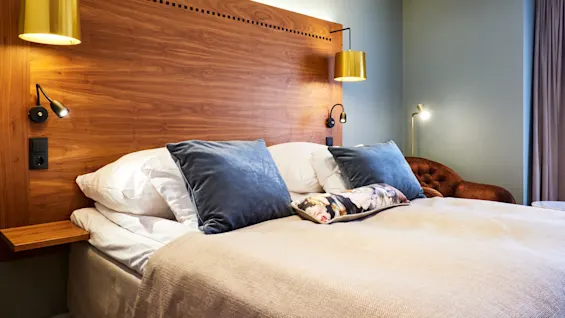 A cozy bedroom with a large bed, plush pillows, wooden headboard, wall-mounted lamps, and a muted color scheme.