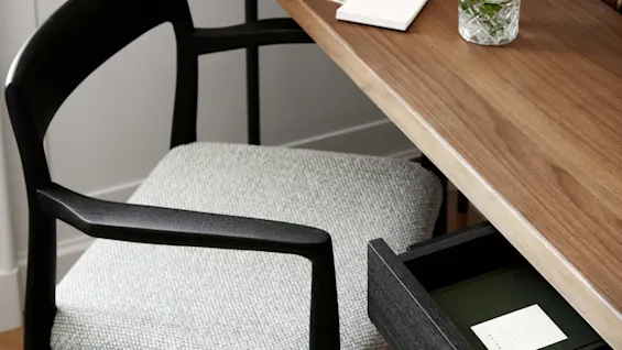 A wooden desk with a drawer slightly open holds a card labeled "NORTEK." A chair is positioned nearby and a glass with herbs and cucumber sits on the desk.