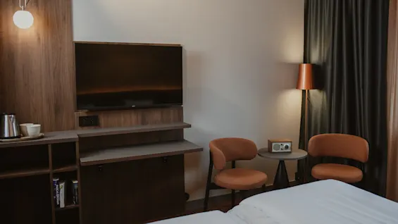 Et velutstyrt hotellrom med en stor TV, et sitteområde med to stoler og en komfortabel seng, perfekt for et avslappende opphold.