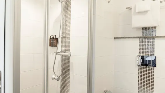 Ett rent och modernt badrum med dusch, toalettartiklar, vit- och gråkaklade väggar och fräscha handdukar.