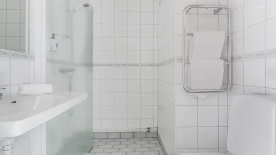 A clean, white-tiled bathroom featuring a sink, shower area, toilet, and a towel rack with fresh towels.
