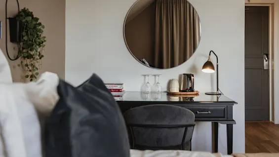 Hotellihuone, jossa on työpöytä, tuoli ja peili. Pöydällä on kirjat N SCHULMAN ja Tage, vedenkeitin ja lasit.