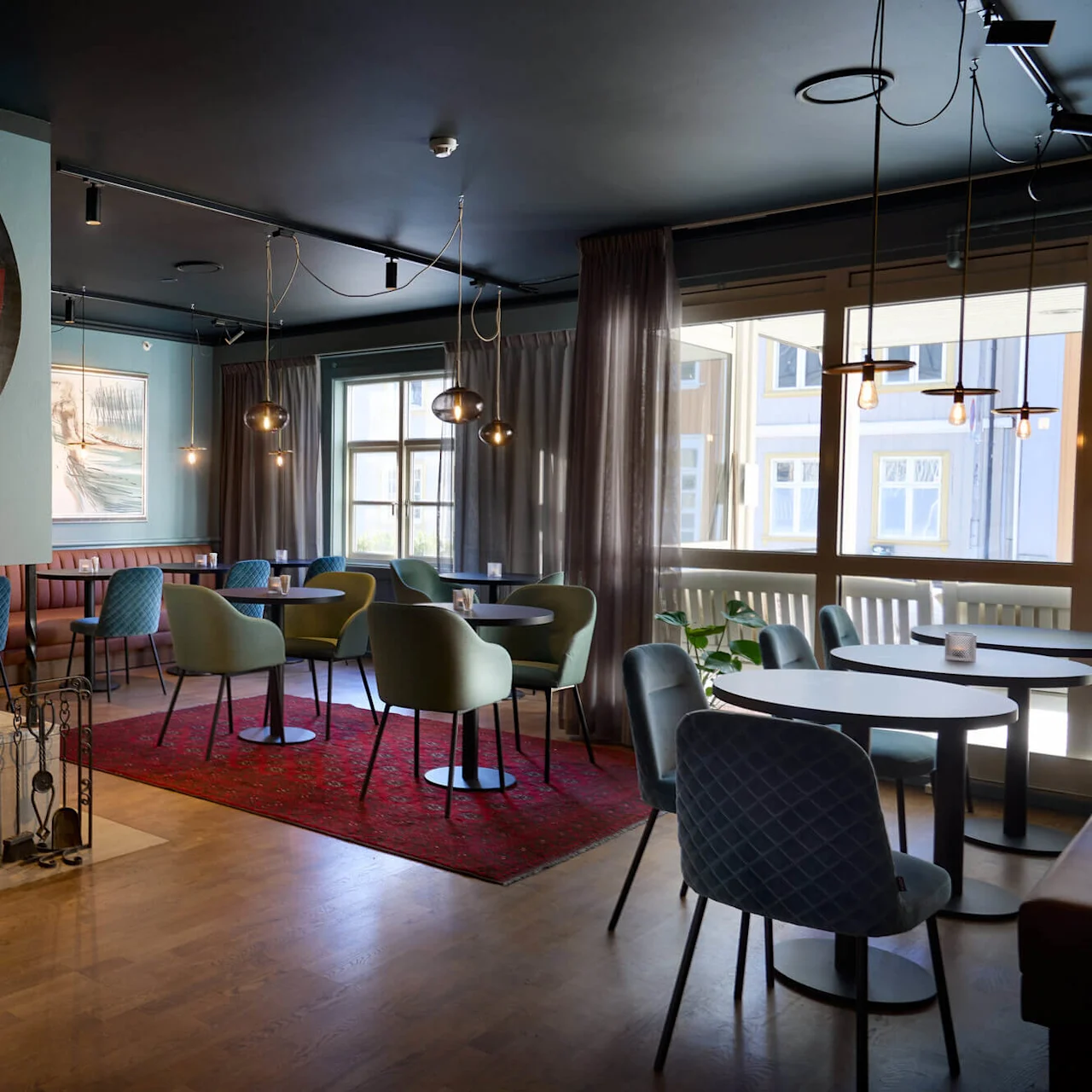 En hyggelig lounge med stilfulde stole omkring borde, en pejs, og moderne hængende lamper i en elegant indendørs indstilling.