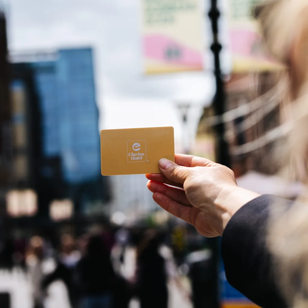 A hand holds a golden hotel card against a blurred city background, suggesting travel or urban exploration.