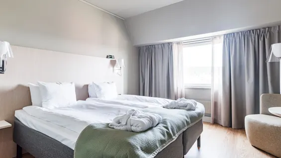 A bright and inviting hotel room with two beds, fresh white linens, and bathrobes, ready for a comfortable stay.