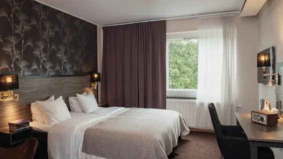 Rauhallinen hotellihuone, jossa on mukava sänky, oma työtila ja ikkuna, josta avautuu rauhallinen luontonäkymä.