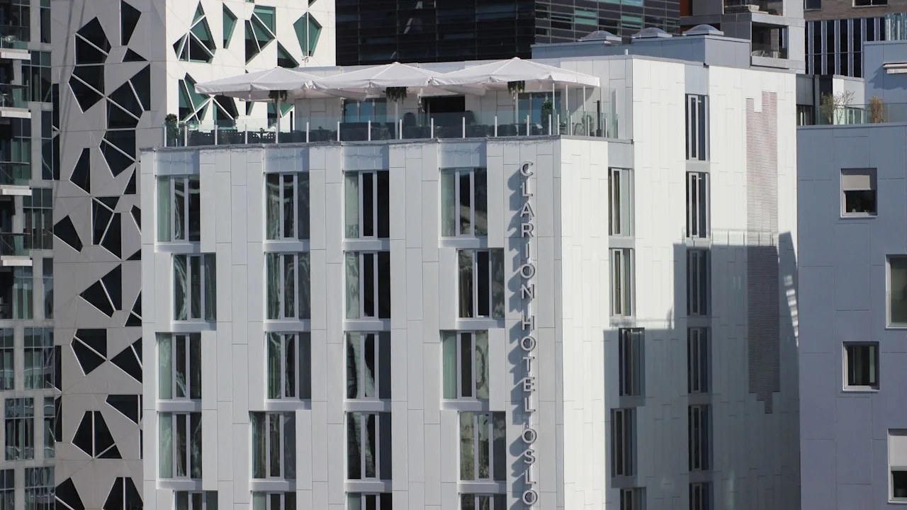 A modern building with a rooftop terrace and umbrellas, featuring "Hotel Oslo" text on its side. Adjacent to a building with a geometric facade.