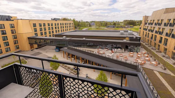 Träbyggnader inramar ett uteserveringsområde; sett från en balkong, med fokus på samtida arkitektur i en stadsmiljö.