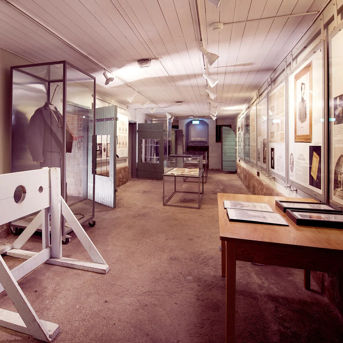 A museum exhibit featuring a wooden guillotine replica, informative displays, and artifacts, conveying history in an indoor, well-lit space.