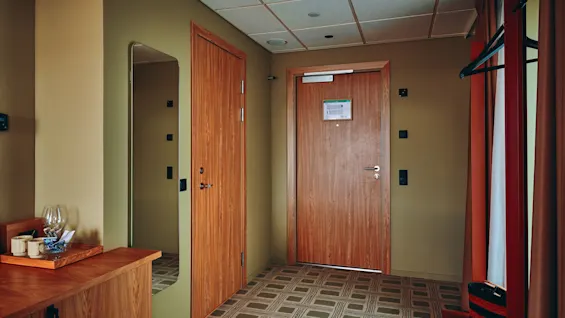 En innbydende hotellromsinngang med varme tredører, et speil og en praktisk plass for eiendeler.