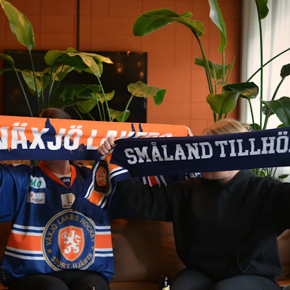 Tva supportrar som haller upp halsdukar i en sofa med texten Smaland tillhor oss
