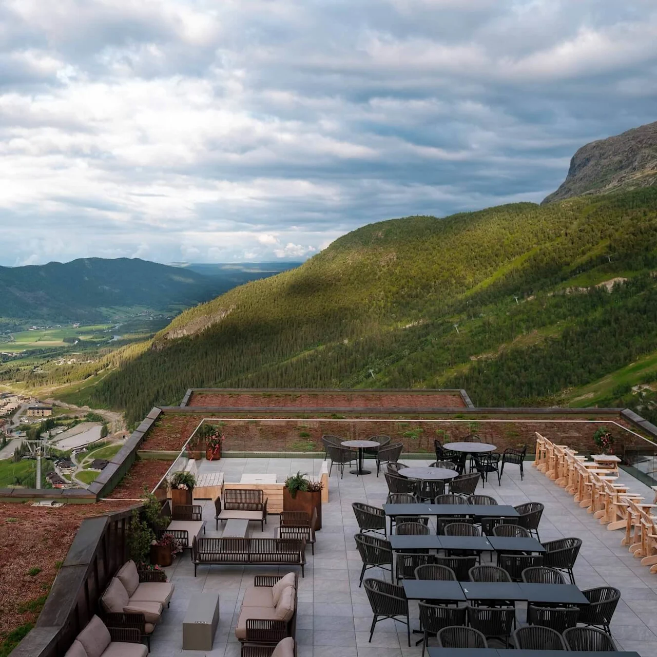 Rooftop terrace featuring modern outdoor furniture, standing still, overlooking a lush green valley with distant mountains and a small town below.