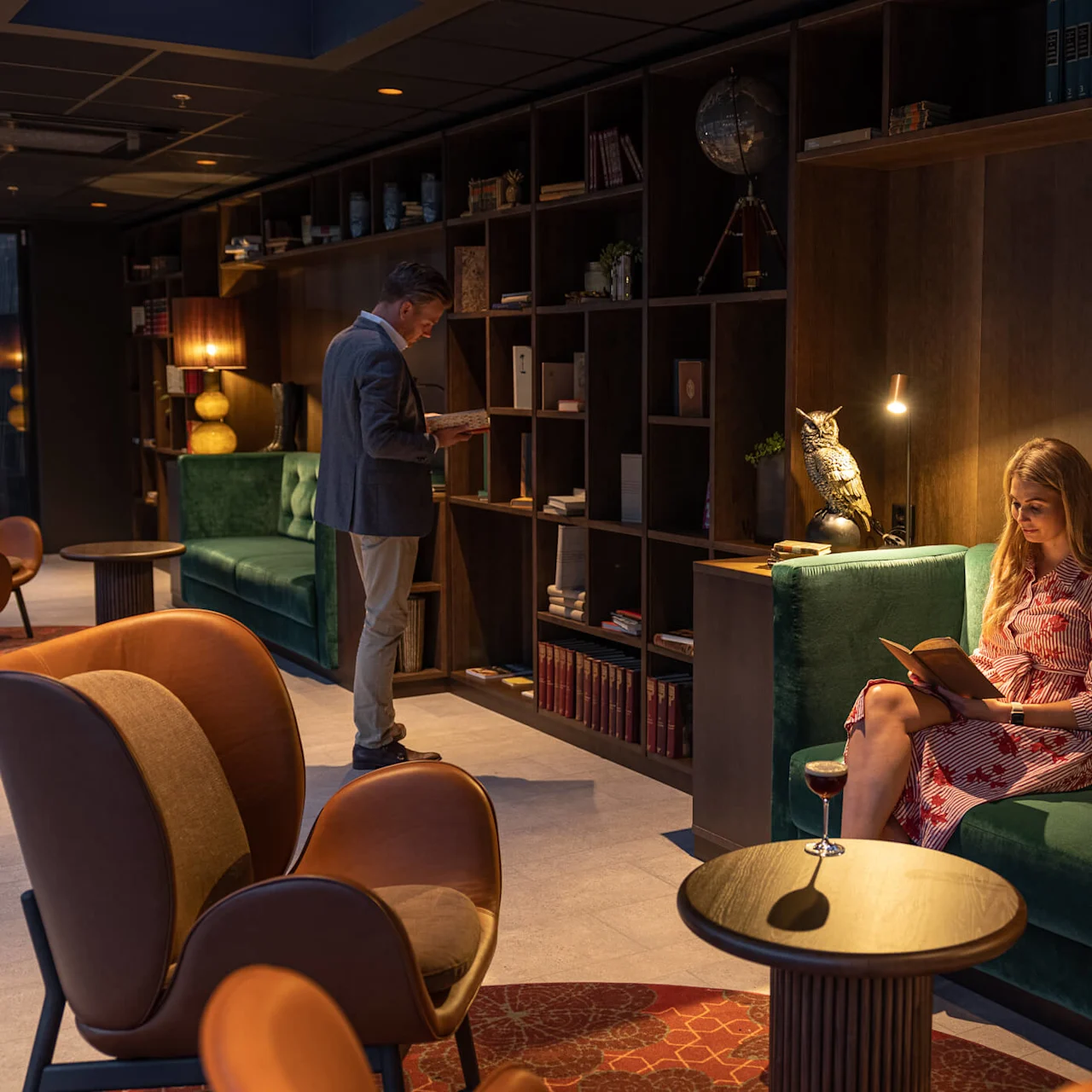Svenska: En man läser och en kvinna sitter med en bok i en elegant lounge, varm belysning, hyllor och stilfulla möbler.