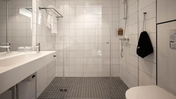 Et moderne badeværelse med walk-in bruser, hvid forfængelighed, og spejlet skab, der udstråler renlighed og minimalisme.