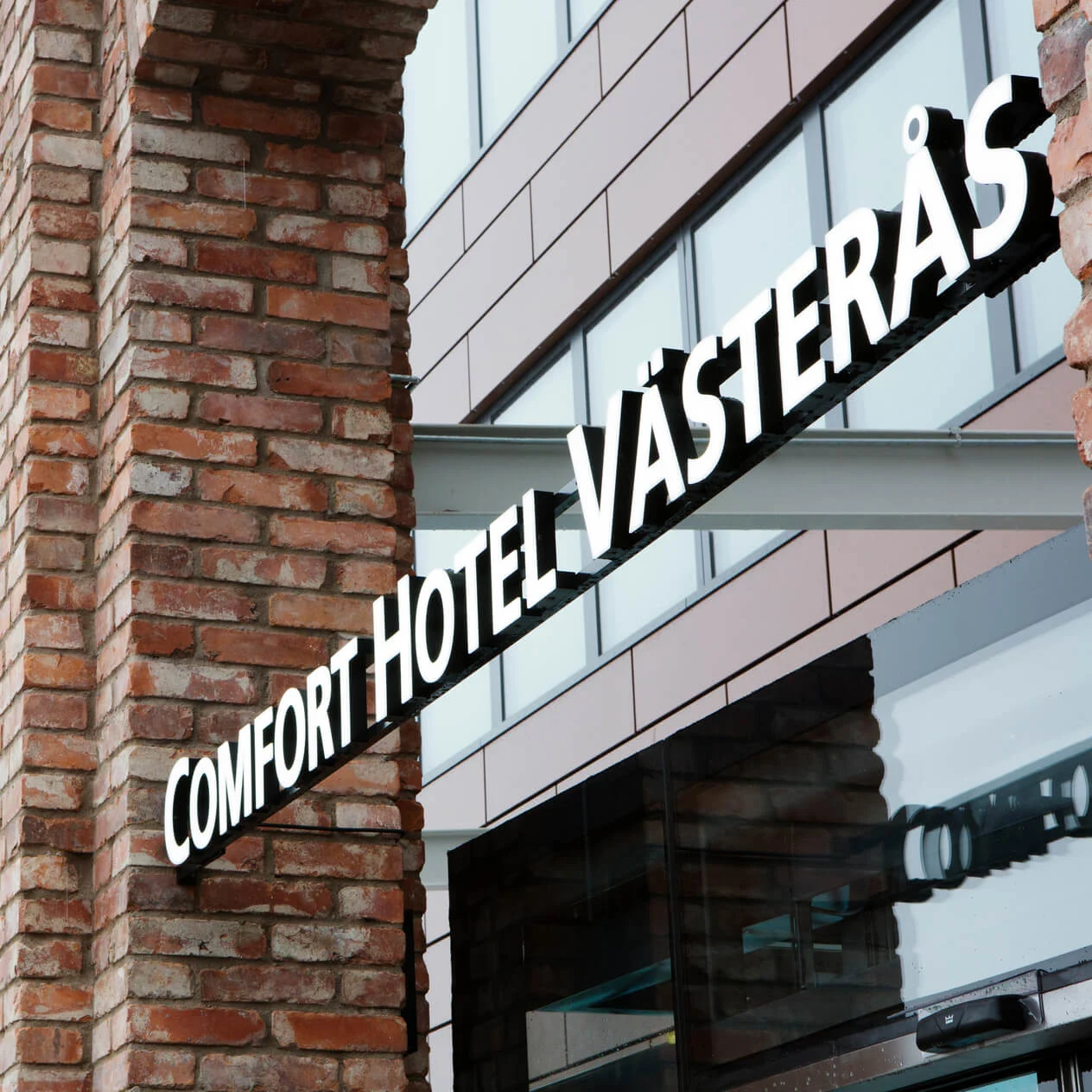 Tegelbyggnadshörn med skylt som läser ”COMFORT HOTEL VÄSTERÅS” i stadsmiljö.
