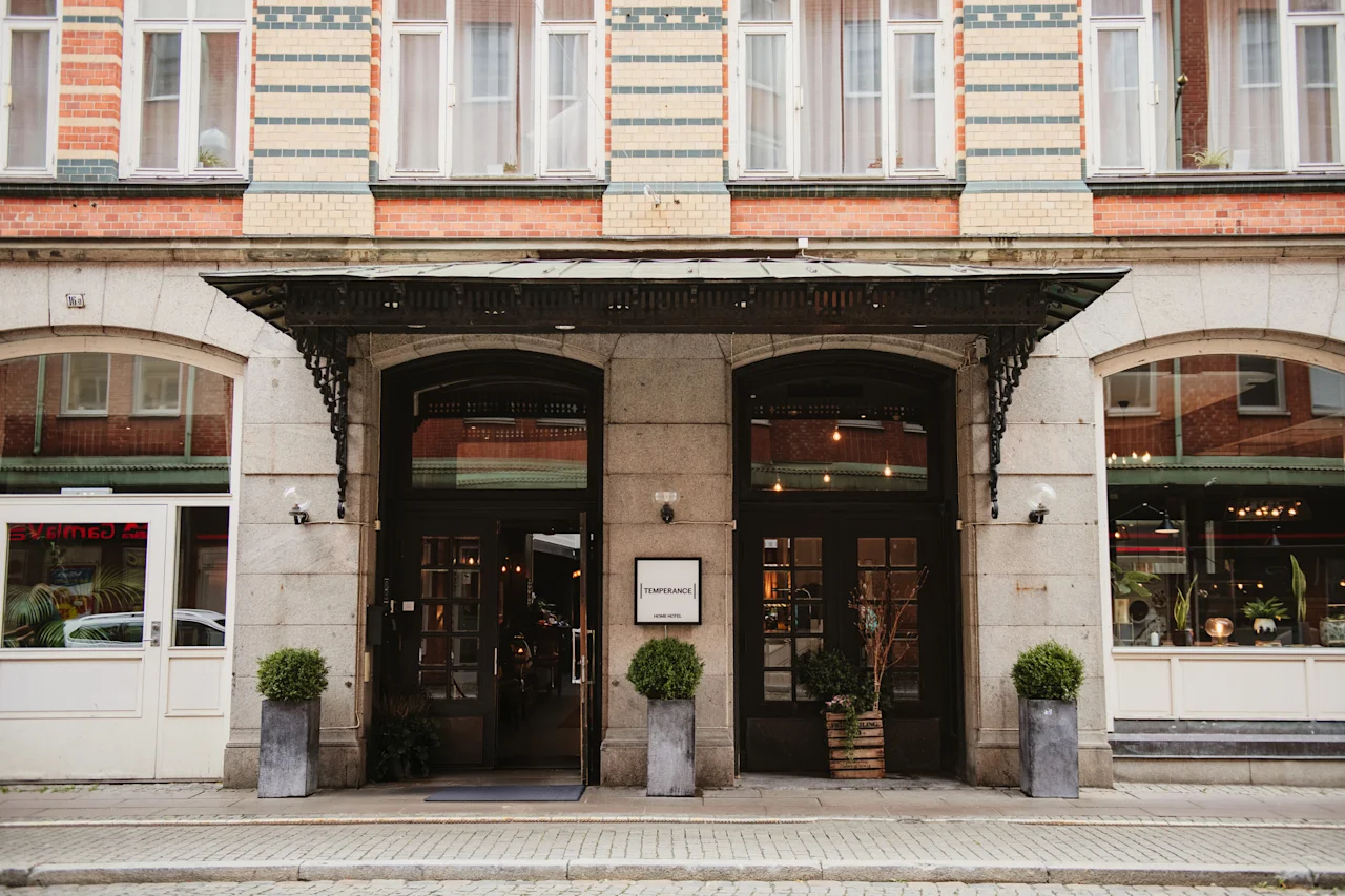 En charmerende bygningsindgang med to mørke døre, en udsmykket markise og potteplanter. Et skilt læser TEMPERANCE HOTEL.