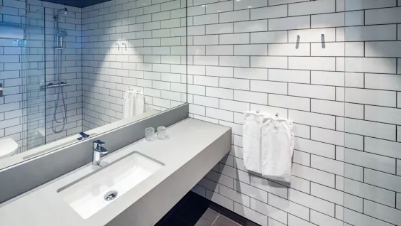 Elegant servant med krom kran, plassert i et bad med hvite t-banefliser. I nærheten er det en glassdør til dusjen og et speil som bidrar til den moderne settingen.