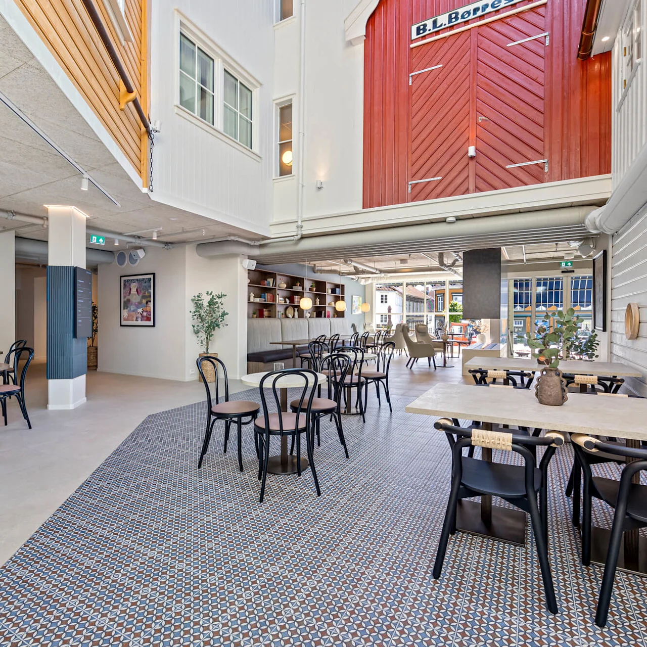 Metal chairs and tables arranged on patterned floor, resembling a modern cafe setting within an indoor space with natural light entering from windows.