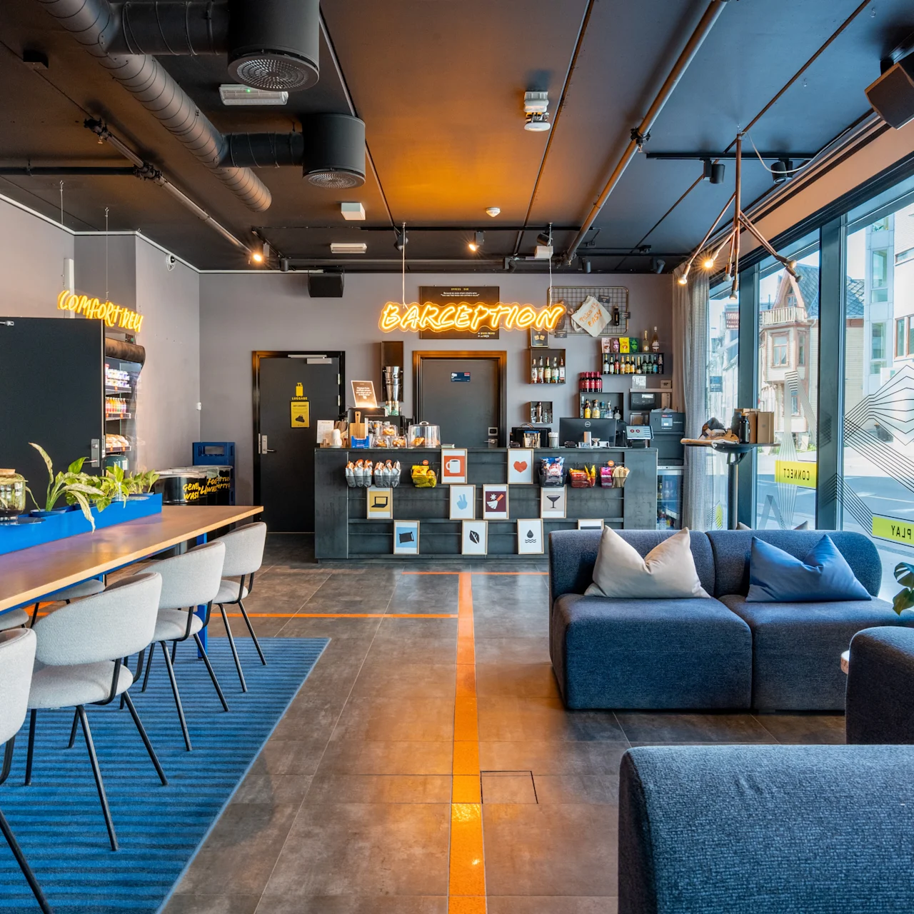 Moderni hotellin aula tyylikkäillä kalusteilla ja sisustuksella. Vastaanottotiski, jossa neonkyltti "CAFEPTION", ympärillään kaupunkimaisema suurien ikkunoiden läpi, mukavat istuimet ja modernit riippuvalaisimet.