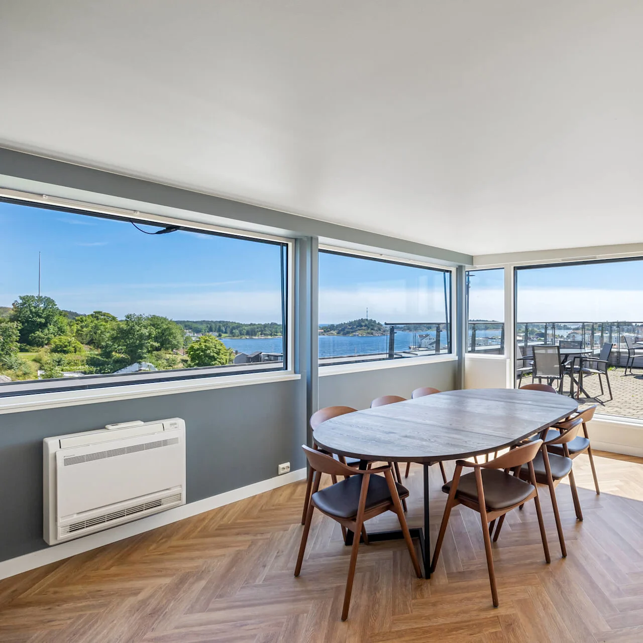 A dining area with a wooden table and chairs, opening onto a balcony with a waterfront view.