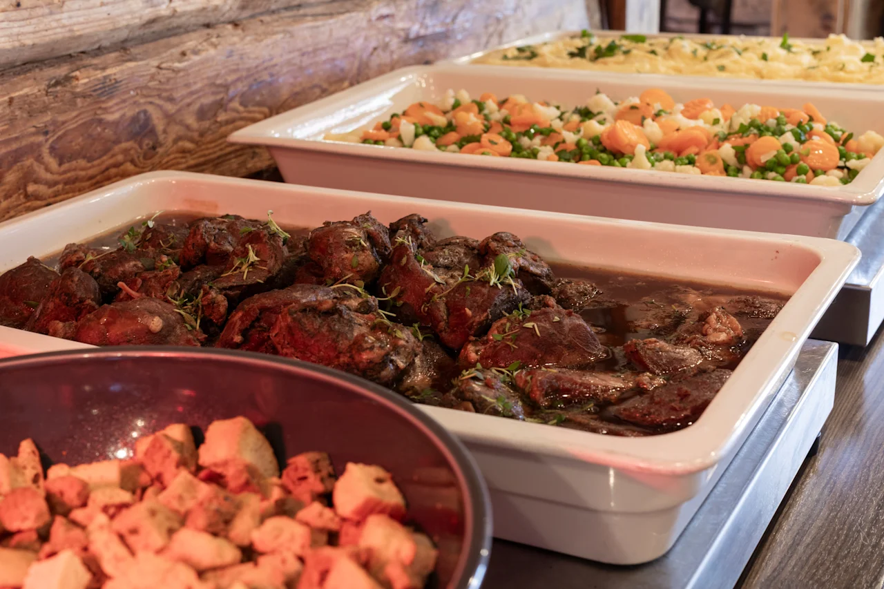 En varm buffetlinje med forskellige tilberedte retter, herunder en solid gryderet, farverige grøntsager og sprøde toppings.