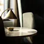 A warm, sunlit indoor scene with a stylish lamp on a table next to a comfortable chair, creating a cozy atmosphere.
