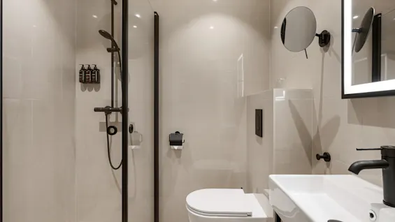 Et moderne badeværelse med bruser, toilet og håndvask, med elegante sorte armaturer og lyse fliser.