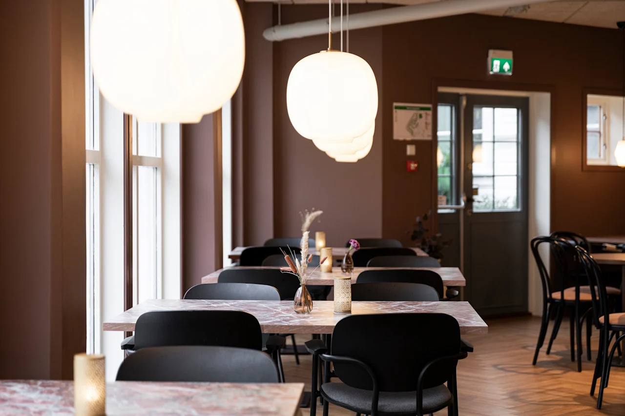 A cozy restaurant dining area with several tables set, warm lighting, and large windows, ready for guests. 🍽️✨