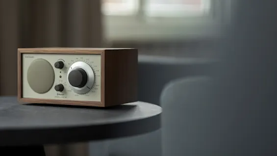 A wooden radio with a speaker and tuning dial sits on a dark table. Text on the radio reads Bluetooth and Model One.