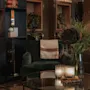 En mysig hotellounge med en grön fåtölj, ett soffbord med tända ljus och blommor, samt dekorativa hyllor. Home Hotel Grand, Helsingborg.