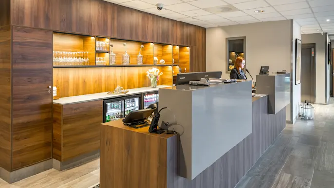 Receptionist working at a modern hotel check-in desk with wooden features and shelving.