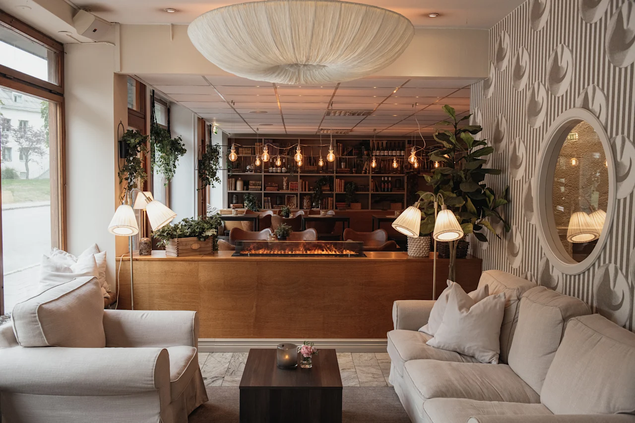 A warm and inviting hotel lounge with comfortable sofas, a fireplace, bookshelves, and decorative lighting.