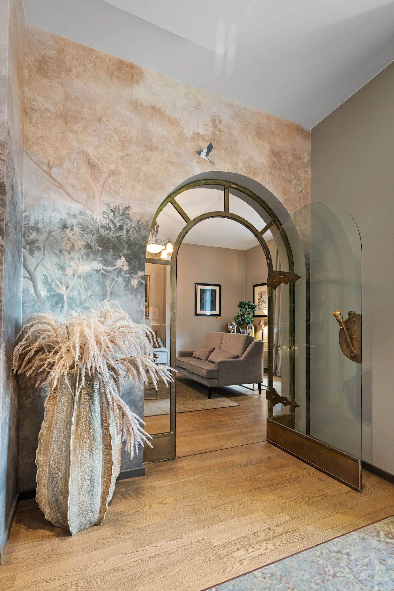 En buet døråpning på Home Hotel Gabelshus åpner inn til et koselig rom med en sofa, med et naturmaleri og tørkede planter.