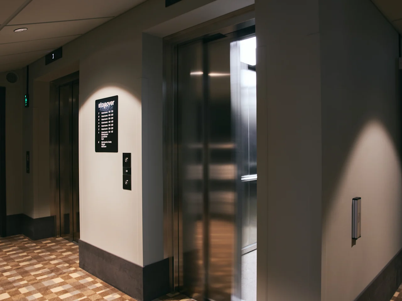 En godt opplyst heislobby på et hotell, med en åpen heis og en etasjekatalog. Tekst: 1 Resepsjon, 2-7 Konferanse, 8 Treningsstudio, 9 Takterrasse.