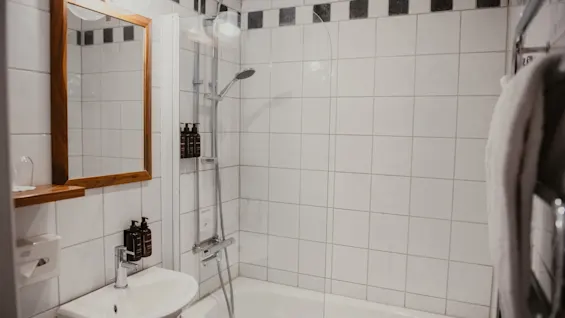 Et lyst og funktionelt badeværelse med bruser over badekar, håndvask og spejl, klar til brug.