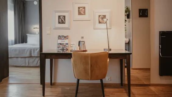 Ett hotellrum med skrivbord, stol och vattenkokare. En lampa lyser upp skrivbordet. En säng syns genom en öppen dörröppning. Text: TROMSO.