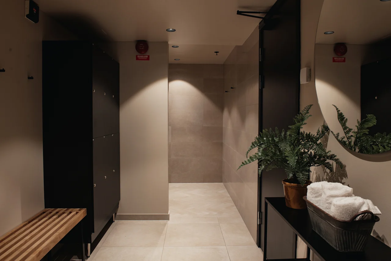 Home Hotel Uppsala's changing room with lockers, a wooden bench, and a plant. Rolled towels and a 'BRANDSLÄCKARE' sign are visible.