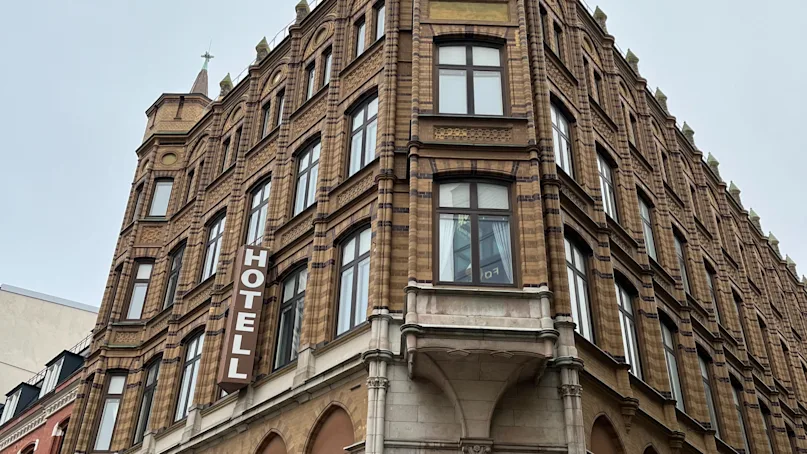 A multi-story, brick hotel building with intricate architectural details displays the word "HOTELL" vertically on its facade. Shops named "Mulberry" and "ETON" are on the ground floor.